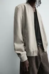 Cazadora bomber negra de corte regular fit, confeccionada en tejido efecto ante. Cuenta con cuello, puños y bajo en rib elástico, manga larga, bolsillos de vivo en la cadera y un bolsillo interior. Cierre frontal con cremallera.