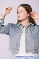 Campera de jean de lavado celeste claro, con diseño clásico de cuello y botones metálicos. Presenta detalles de pequeños brillos o tachas plateadas sobre la tela, especialmente visibles en los bordes de los bolsillos y costuras.