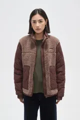 Campera de diseño híbrido que combina paneles de corderito sintético en color crema con mangas y bolsillos de tela técnica acolchada en color verde militar. Presenta cierre frontal completo, cuello alto y un pequeño parche decorativo en el pecho.