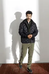 Campera puffer negra con capucha, diseño de costuras horizontales y verticales que crean un efecto de bloques, cierre frontal completo y bolsillos laterales.