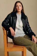 Campera tipo gamulán de cuero sintético negro con interior y detalles de cuello y puños en corderito negro. Presenta cierre frontal y diseño oversize.