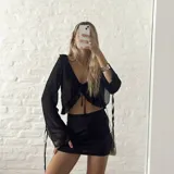 Blusa corta negra de mangas largas acampanadas, con volados en el escote y lazo ajustable en el frente.