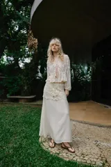 Blusa de escote en pico y manga larga con puños elásticos. Presenta un diseño semitransparente con bordados florales a tono, cintura elástica y cierre frontal mediante lazos con abalorios decorativos.