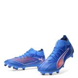 Championes de fútbol Puma Ultra Match para terreno firme, en color azul con detalles en blanco y naranja. Presentan un diseño de corte medio con tejido técnico ligero y suela con tapones para tracción en césped natural.