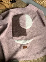 Campera de textura tipo bouclé en color rosa, con diseño de apliques abstractos en tonos marrón y blanco. Presenta un parche de cuero sintético con la marca en la parte inferior.