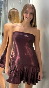 Vestido corto strapless de lurex en color bordó, con diseño ajustado en el torso y falda con doble volado en el ruedo.