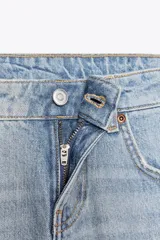 Jeans de tiro bajo con diseño wide leg y corte full length. Presenta cinco bolsillos, cierre frontal con cremallera y botón metálico, en un lavado de denim claro.