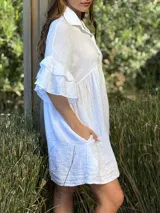 Vestido camisero blanco de lino italiano, con cuello camisero, cierre frontal con botones, mangas cortas con doble volado y bolsillos laterales.