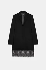 Vestido tipo blazer negro, de corte recto y largo medio, con cuello solapa, manga larga con abertura y botones, y bolsillos con solapa en el delantero. Presenta un bajo con aplicación de encaje negro a tono.