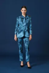 Saco de mujer con diseño de smoking, estampado con patrón de plumas en tonos azules. Presenta solapas clásicas, cierre frontal con botones y puños con detalle de botones dorados. La prenda incluye una blusa a juego con lazo en el cuello.