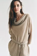 Camisa de cuello fluido y manga larga con puños anchos, de corte recto y largo medio, confeccionada en tejido rústico en tono beige con sutil textura jaspeada. Cuenta con un cinturón ajustable del mismo género para entallar la cintura.
