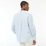 Camisa de popelina celeste con finas rayas blancas verticales, de manga larga, cuello camisero y cierre frontal con botones.
