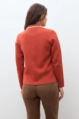 Chaqueta tejida de punto color naranja, con cuello camisero, cierre frontal de botones y dos bolsillos frontales con solapa. Presenta detalles de bordado en contraste en el cuello y los bolsillos.