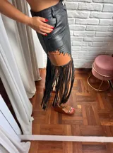 Pollera midi de cuero negro con inserción marrón y costuras decorativas tipo cordón, rematada con largos flecos negros.