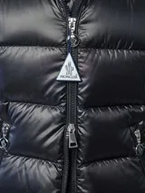 Campera puffer Moncler modelo Glesse, color negro, con diseño acolchado horizontal, capucha ajustable, cierre frontal y bolsillos laterales con cierre. Cuenta con un bolsillo con solapa y parche del logo en la manga izquierda.