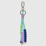 Llavero decorativo con cordones de color turquesa, adornado con cuentas de plástico en tonos lila, azul y amarillo, y rematado con terminales metálicos.