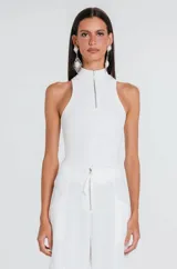 Musculosa de tejido canelado en color blanco, con cuello alto y cierre frontal parcial con cremallera dorada. Presenta un diseño ajustado al cuerpo y sisas amplias.