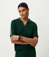 Blusa femenina de punto color verde oscuro, con cuello polo y abertura delantera sin botones. Presenta una trama ahuecada con textura uniforme y mangas cortas con detalle de rayas blancas en los hombros. El modelo es recto y de largo regular.