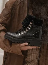 Borcego de cuero vacuno color negro, con suela de goma track, cordones y detalles en corderito sintético en la lengüeta y zona del tobillo. Cuenta con ojales metálicos y textura en relieve en la parte trasera.