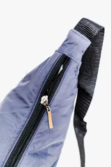 Bandolera color gris claro con forma de media luna, cierre de cremallera y correa ajustable. Incluye etiqueta metálica con el logo de la marca.