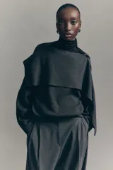 Pantalón sastrero gris oscuro de corte holgado con tiro alto, cierre con corchete y botón ocultos. Presenta piernas amplias con pinzas, raya marcada en el frente y la parte trasera, bolsillos al bies y bolsillos decorativos en la parte posterior.