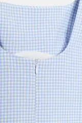 Vestido corto de tirantes anchos con lazada en los hombros, escote cuadrado y cierre de cremallera oculta en la espalda. Presenta un estampado de cuadros vichy en tonos celeste y blanco.