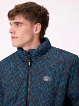 Campera reversible de nylon con cuello alto y cierre frontal. Un lado es de color gris liso con logo bordado, mientras que el otro lado presenta un estampado abstracto en tonos azules. Cuenta con bolsillos laterales y puños elásticos.