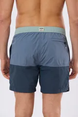 Short de baño con diseño de bloques de color en tonos celeste y azul marino, con cintura elástica en color verde claro y cordón ajustable.