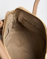 Cartera chica tipo handbag de color beige, con textura granulada, doble asa superior, correa ajustable y desmontable, herrajes metálicos dorados y detalle de llavero colgante con forma de borla. Cuenta con cierre superior y logo de la marca estampado en el frente.