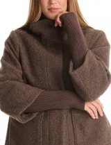 Tapado de tejido bouclé color marrón, con silueta evasé y largo a la cadera. Presenta cuello alto envolvente, cierre frontal oculto con botones a presión y bolsillos frontales de gran tamaño. Sus mangas son 3/4 con corte amplio y puños de tejido rib al tono que se extienden para cubrir las muñecas.