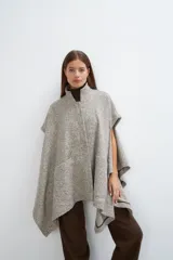Capa de lana fina con cuello alto, cierre frontal con botones ocultos y bolsillos plaqué. Presenta aberturas laterales versátiles que permiten usarla como poncho o ruana, con terminaciones envivadas.