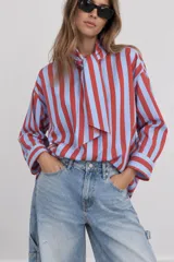 Camisa de manga larga con diseño de rayas verticales en tonos rojo y celeste, corte holgado y cuello con lazo incorporado para atar.