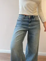 Pantalón de jean con corte wide leg y tiro medio-alto. Presenta un lavado gris azulado desgastado con acabado vintage y ruedo desflecado.