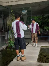 Chomba de piqué con diseño color block vertical en negro y verde oscuro, cuello polo y cierre frontal parcial. Presenta inscripciones en el frente.