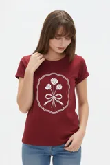 Remera de manga corta color bordó con cuello redondo a la base y estampado gráfico en el centro de rosas con moño dentro de un marco ondulado blanco.