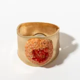 Brazalete rígido dorado con aplique central de piedras rojas y naranjas.