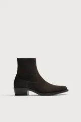 Bota estilo cowboy de caña corta para hombre, confeccionada en piel con acabado serraje de color marrón oscuro. Presenta diseño liso con punta ligeramente cuadrada y tacón bajo, incorporando costuras decorativas laterales.