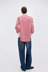 Camisa oversized de popelina de algodón con diseño a rayas verticales rojas y blancas. Presenta cuello clásico y puños anchos en color blanco sólido, cierre frontal con botones y bajo redondeado con aberturas laterales.