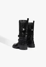 Bota de caña alta color negro, confeccionada en una combinación de cuero liso en la base y material tipo mesh perforado en la caña. Presenta múltiples correas horizontales con hebillas metálicas decorativas y una suela track de goma con taco bajo.