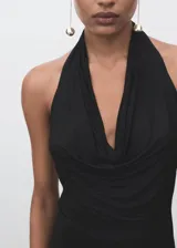 Vestido largo negro de corte entallado, con cuello halter drapeado y espalda descubierta. Presenta una abertura en la parte trasera y diseño sin mangas.