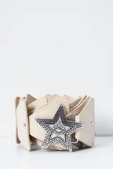 Cinto de cuero color crudo con hebilla metálica plateada en forma de estrella.