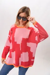Sweater de punto con diseño geométrico abstracto en tonos rosa y rojo, con cuello redondo y puños y bajo acanalados en color naranja.