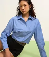 Camisa celeste con rayas verticales blancas, de corte alargado, cuello inglés y mangas largas.