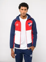 Campera deportiva Umbro del Club Nacional de Football, modelo Summit. Presenta un diseño con bloques de color en azul, rojo y blanco, con capucha, cierre frontal y bolsillos laterales con cierre. Incluye el logo de la marca y el escudo del club en el pecho.