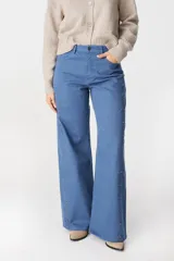 Jean de corte recto y tiro medio, color azul, con detalles de tachas metálicas doradas a lo largo de las costuras laterales externas.