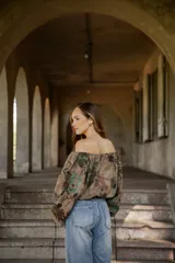 Blusa de lino con diseño off-shoulder, mangas largas amplias y estampado floral en tonos tierra y verdes.