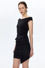 Vestido corto negro en punto texturizado, de corte entallado con hombros descubiertos, escote en V y frunces laterales que generan un efecto drapeado. Cuenta con un nudo ancho asimétrico al frente.