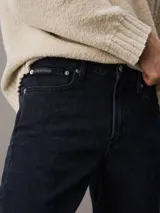 Pantalón de jean negro de corte slim taper, con bragueta con cremallera y diseño de cinco bolsillos.