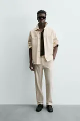 Pantalón chino de corte relajado, color beige claro, con textura de rayas verticales sutiles. Presenta cintura ajustable con cordón interior, bolsillos delanteros y bolsillos traseros de vivo.
