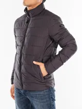 Campera puffer Calvin Klein color gris oscuro, con cuello alto, cierre frontal con cremallera, bolsillos laterales con cierre, puños elásticos y logo en la manga.